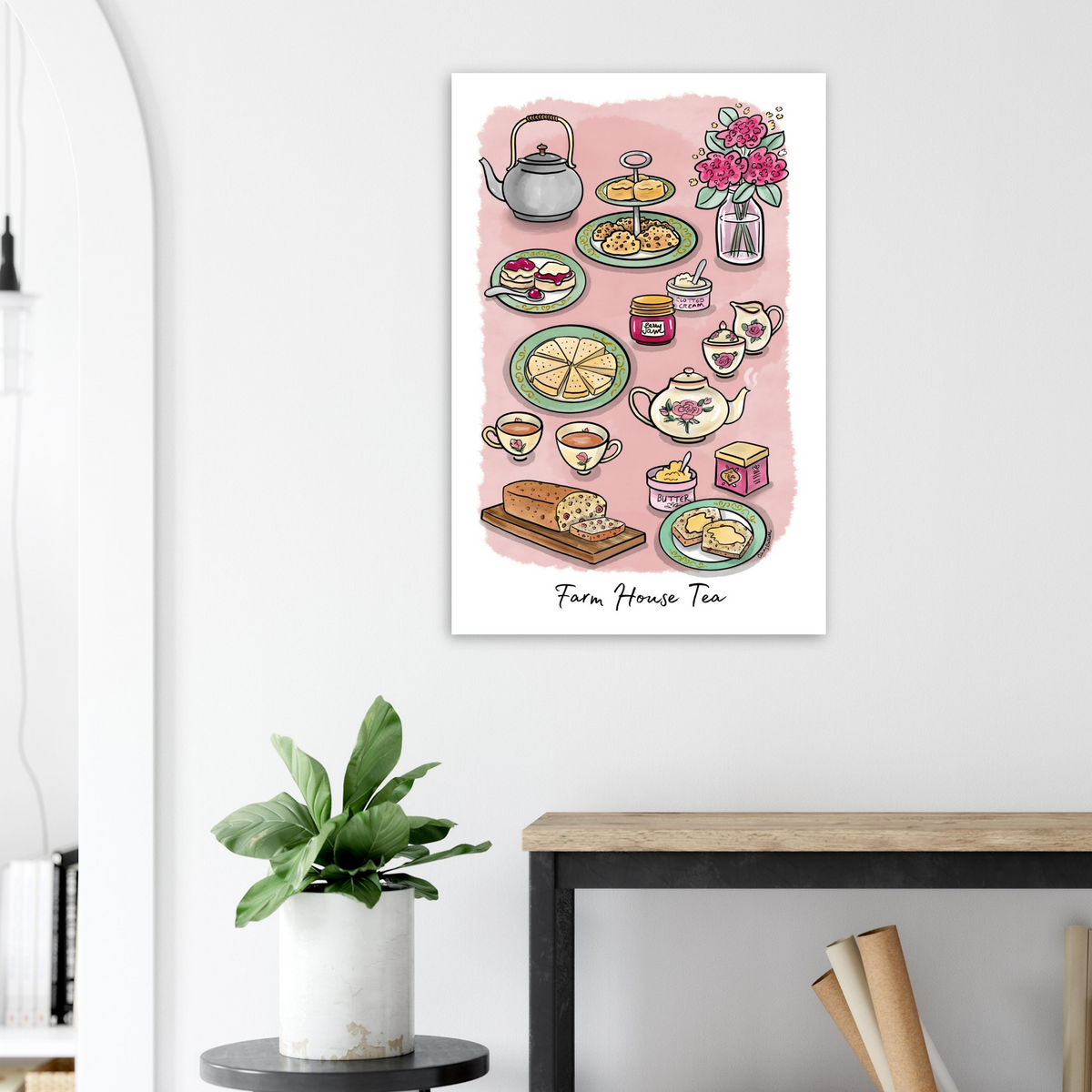 Wall art for cozy tea lover home featuring a colorful watercolor-style illustration of a tea party hanging on a white wall above a small table with a potted plant.