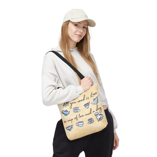 Woman holding tote bag with tea cups, a dog, and the quote 'All you need is love, a cup of tea, and a dog' . Size 13"x13"