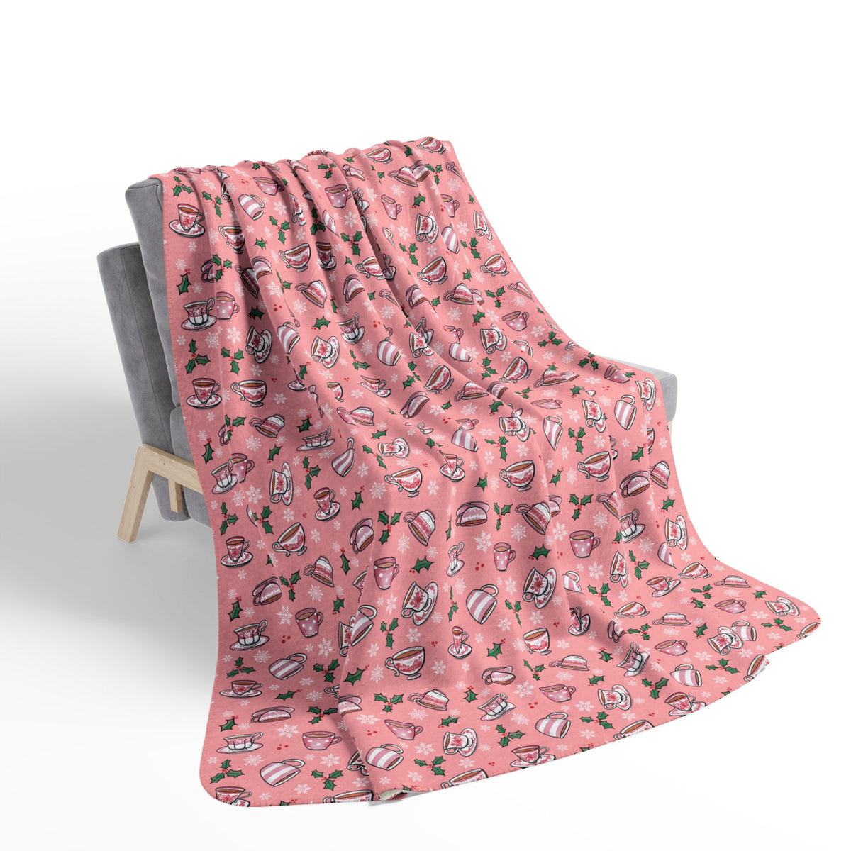 Hand drawn teacups with holly and snowflakes on a soft pink fleece blanket draped on a chair 