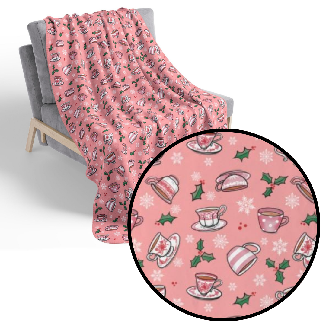 Hand drawn teacups with holly and snowflakes on a soft pink fleece blanket draped on a chair with detail call out
